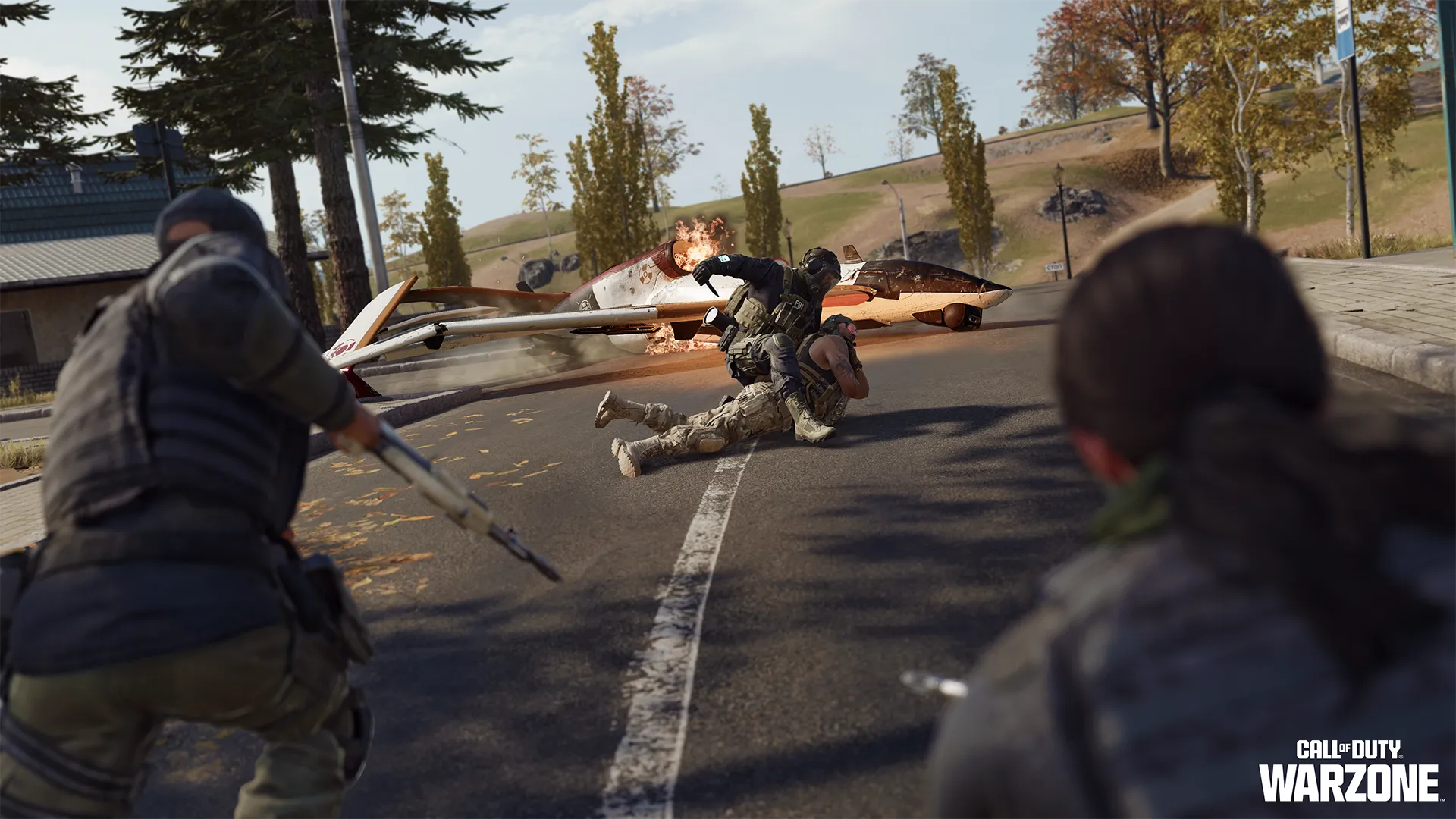 Soldiers struggle beside a crashed burning aircraft on a road lined with autumn trees.