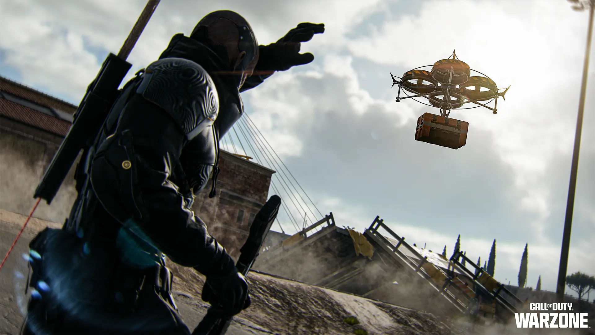 An armored operator watches a cargo drone carrying a supply crate above a damaged urban area.