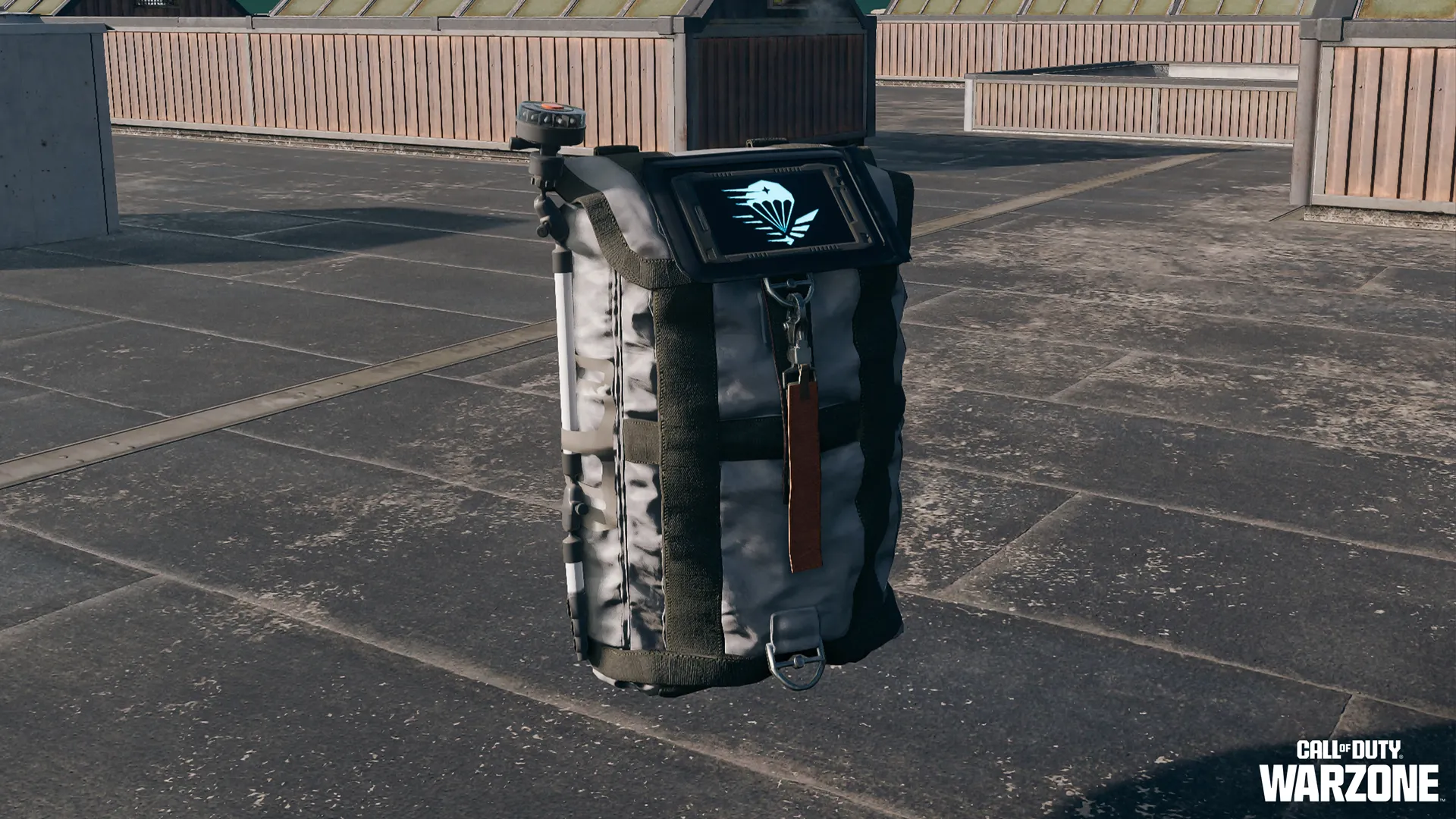 Portable backpack device with a digital display showing a parachute icon, standing on a rooftop.