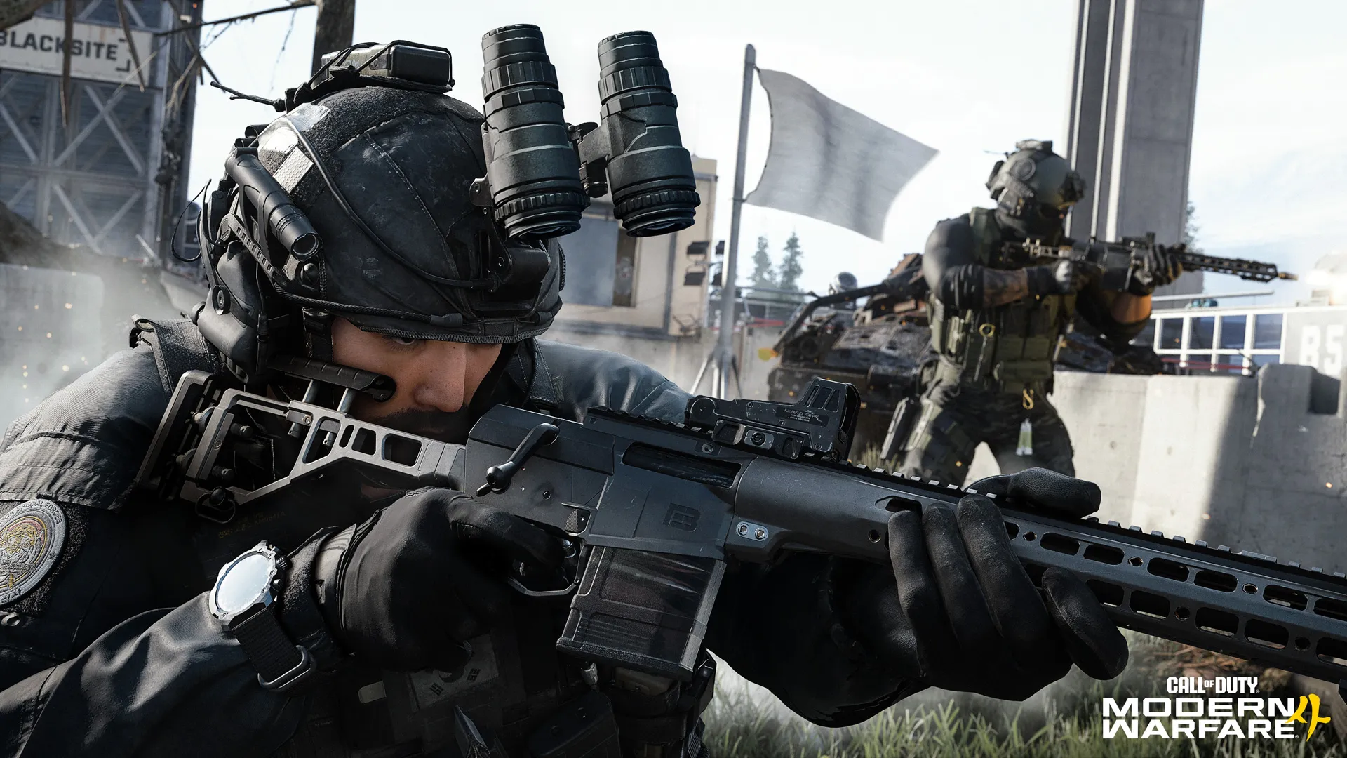 Two black-clad operators aim rifles while advancing through an outdoor military facility.