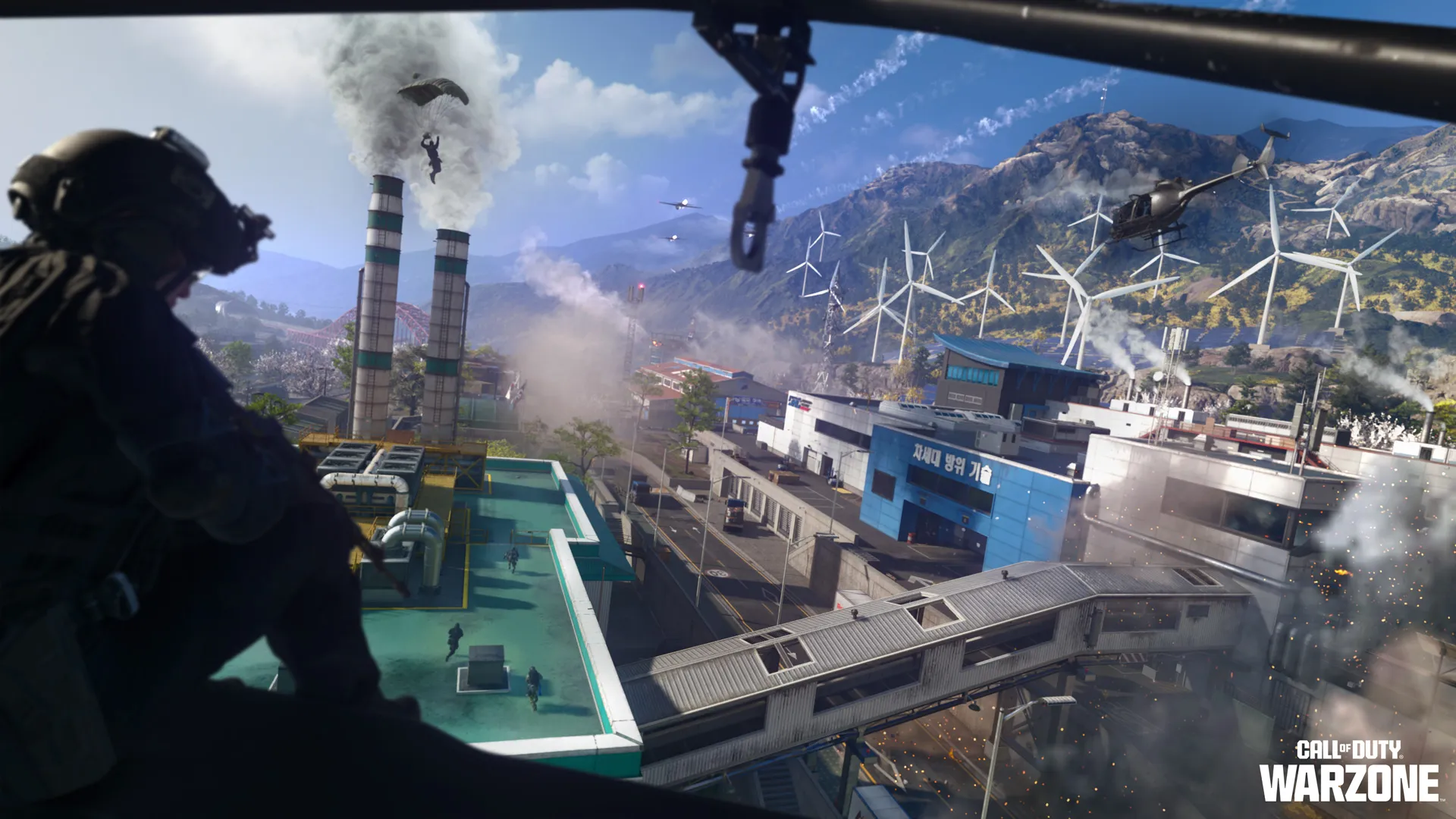 An operator overlooks a sprawling industrial complex with helicopters, parachutists, smokestacks, and wind turbines.