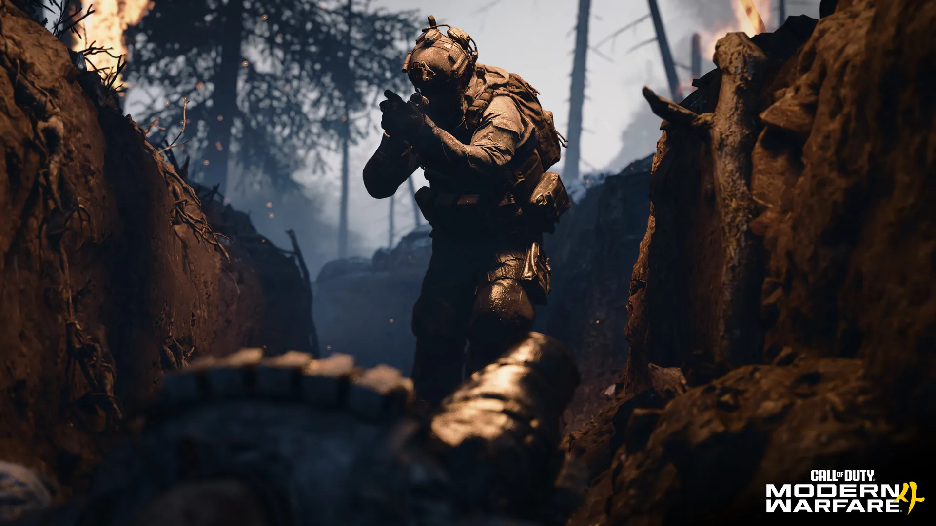 A heavily equipped soldier advances through a muddy trench amid burning trees and drifting embers.