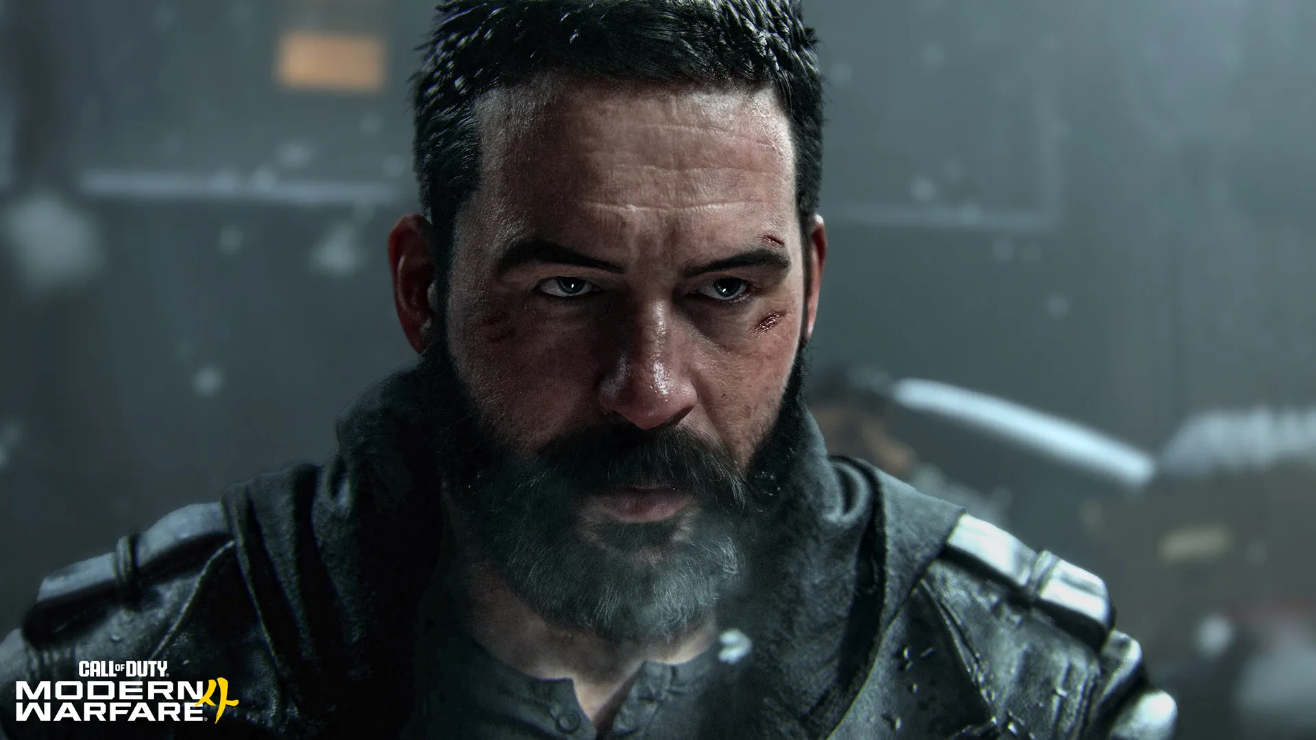 Close-up of a bearded man with short dark hair, facial scars, and a serious expression, wearing dark tactical clothing.