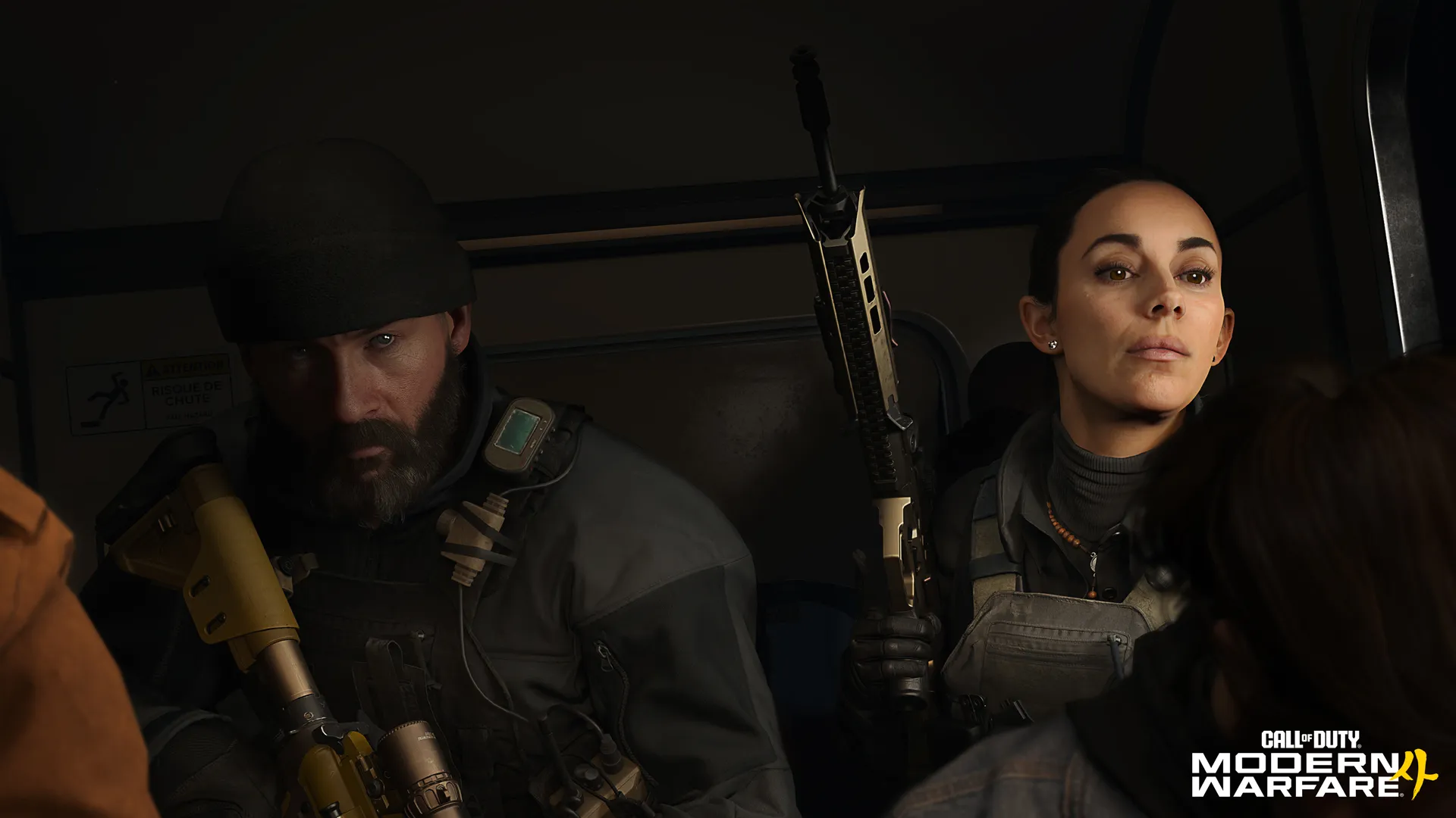 A bearded soldier (Price) and an armed woman (Valeria) sit together inside a dark vehicle.