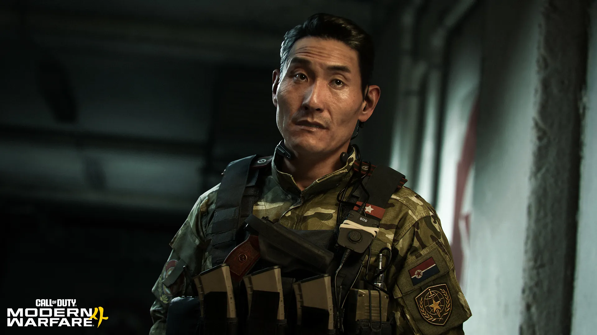 A soldier in camouflage and tactical gear looks upward inside a dim building.