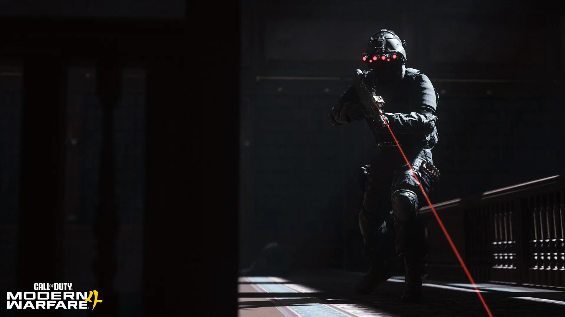 A soldier wearing red-lit night-vision goggles aims a laser-equipped rifle in a dark interior.
