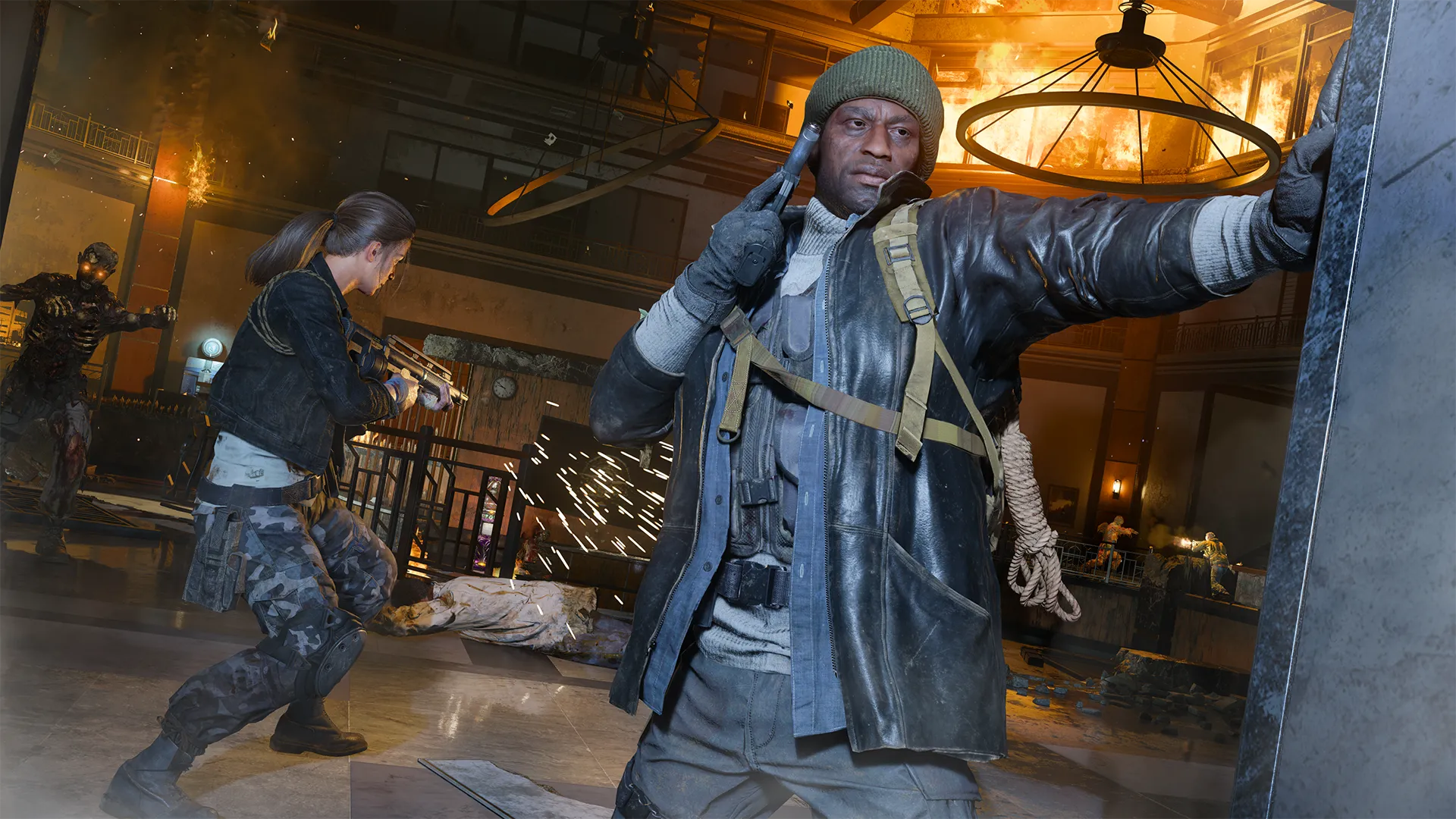 A man (Weaver) in a green knit cap and tactical coat takes cover inside a burning, war-torn lobby while aiming a pistol, as another fighter (Grey) engages zombies in the background amid falling sparks and flames.