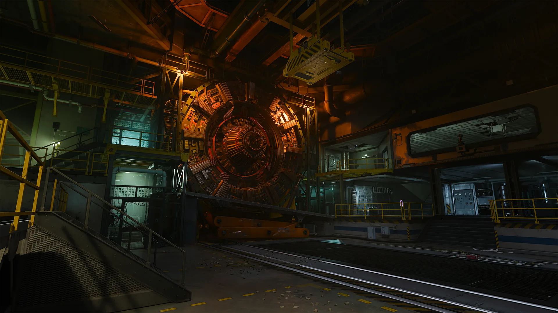 A dimly lit industrial chamber houses a massive circular machine with orange-red lighting, surrounded by metal walkways, catwalks, and control rooms, suggesting a high-tech or experimental facility.