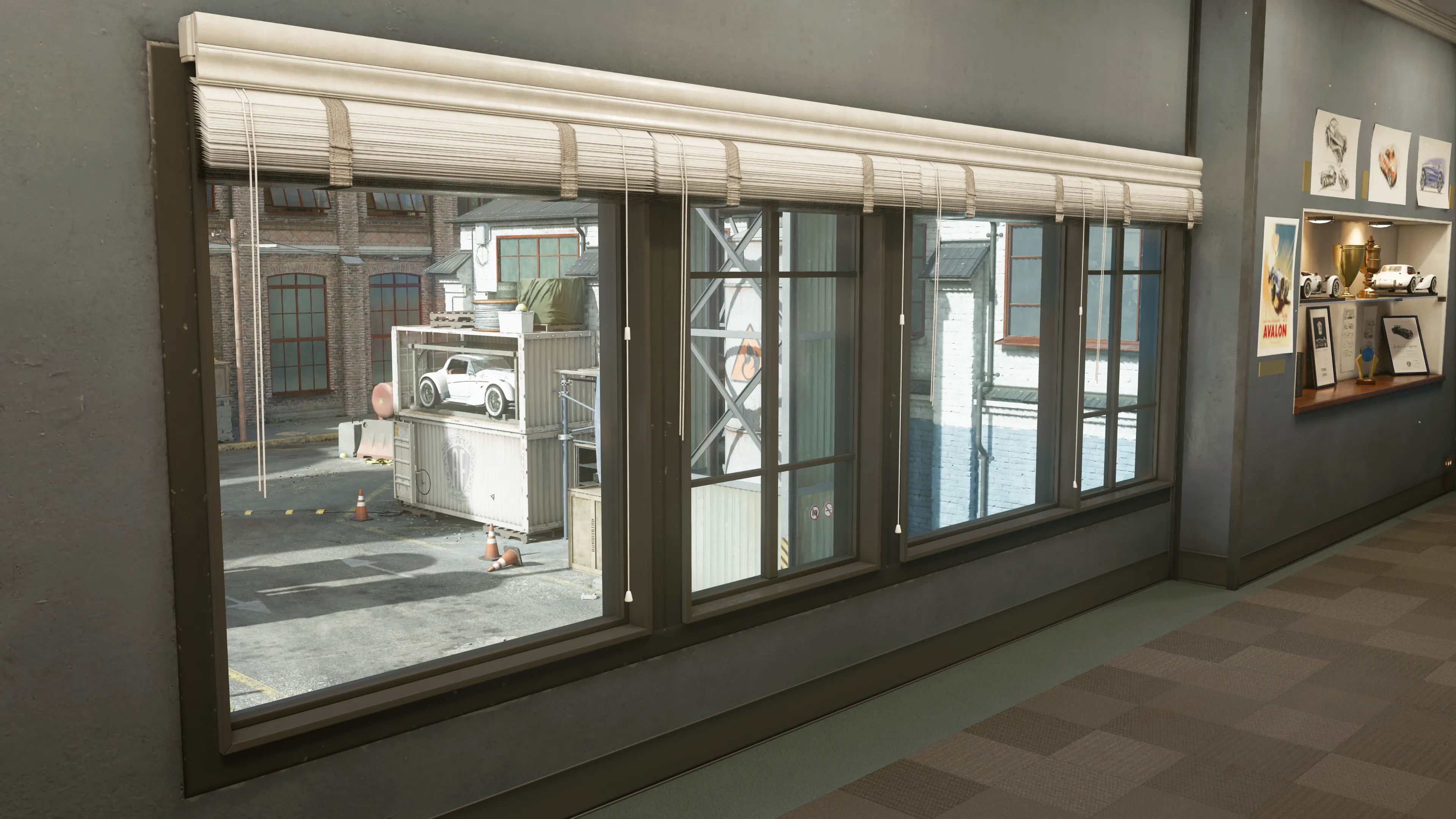 From inside an office, the window view reveals a courtyard with containers, a white car on a raised platform, and a brick factory in the distance. Trophies and framed documents decorate the room. (Description by ChatGPT)